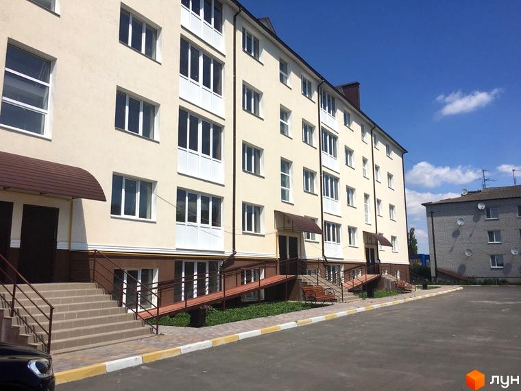 Новобудова ЖК Садовий. Фасад будинку світло-бежевого кольору з білими балконними блоками. Біля будинку розташовані пандуси, сходи та лавка.