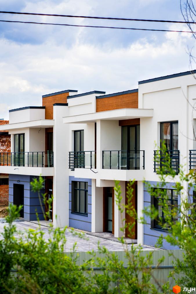 Зовнішній вигляд будинків котеджного містечка КМ City Villa Club з балконами та сучасними фасадами. Прибудинкова територія з бруківкою та зеленню.