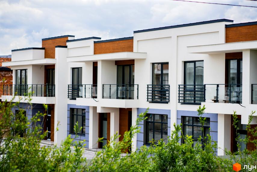 Котеджне містечко КМ City Villa Club – фасади будинків з панорамними вікнами та балконами. Навколо зелені насадження.