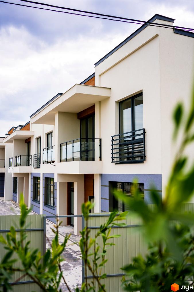 Зовнішній вигляд будинків котеджного містечка КМ City Villa Club з балконами та вікнами. Прибудинкова територія з парканом та зеленню.