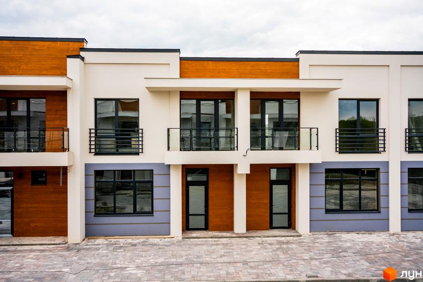 Котеджне містечко КМ City Villa Club. Фасад будинку з дерев'яними елементами, великими вікнами та балконами, вимощена бруківкою прибудинкова територія.