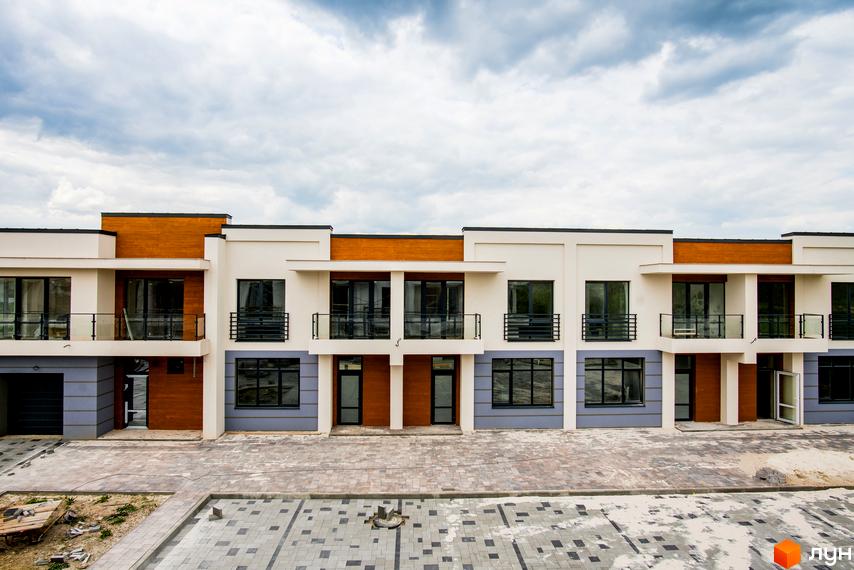 Котеджне містечко КМ City Villa Club. Фасад будівель з білою штукатуркою, дерев'яними елементами та великими вікнами. Прибудинкова територія вимощена плиткою.