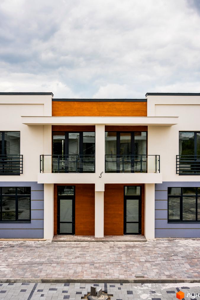 Фасад будинку КМ City Villa Club з великими вікнами та дерев'яними елементами. Перед будинком вимощені доріжки з плитки.