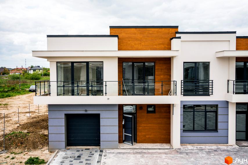 Зовнішній вигляд будинку КМ City Villa Club з гаражем та балконами. Навколо будинку облаштована прибудинкова територія з дорогою та зеленими насадженнями.