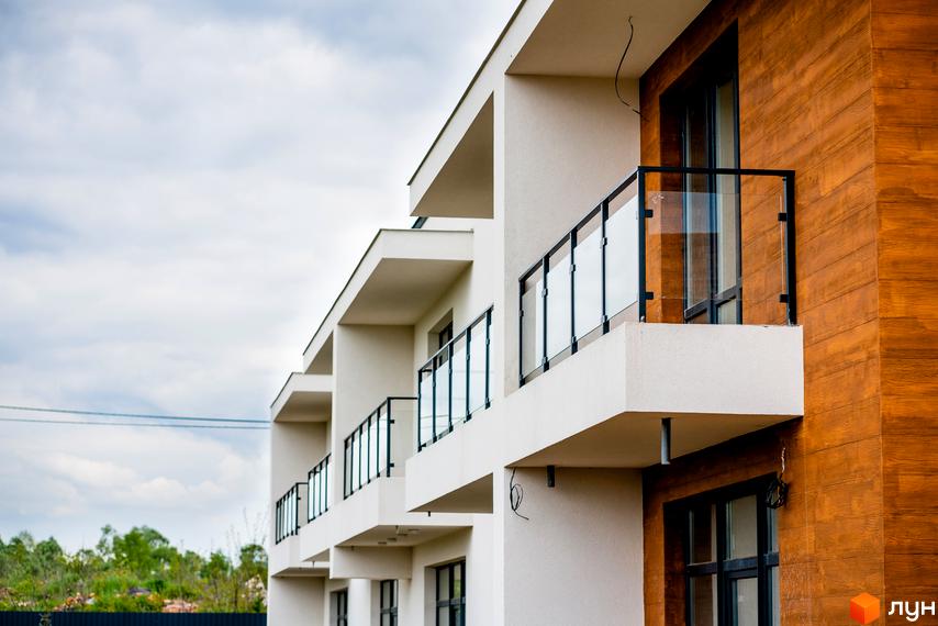 Котеджне містечко КМ City Villa Club: фасади будівель з панорамними вікнами та скляними балконами. Навколо зелені насадження та паркан.