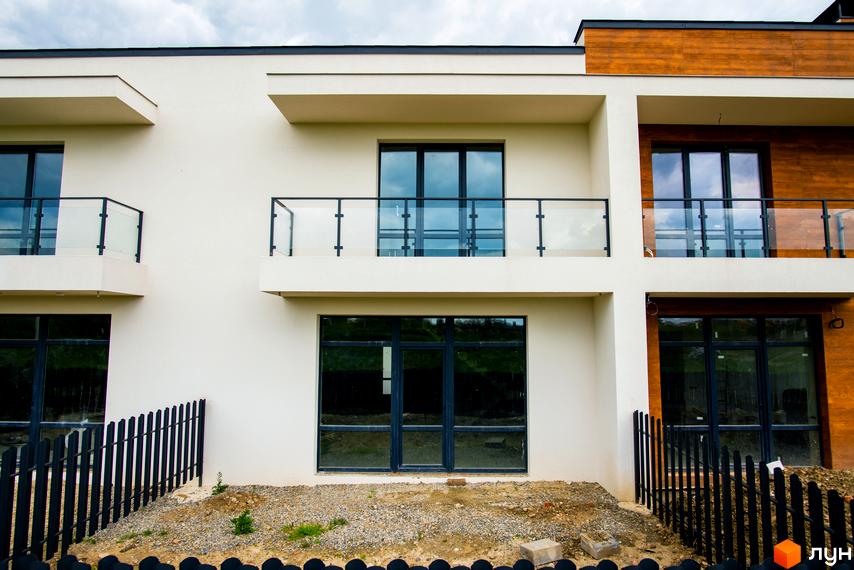 Котеджне містечко КМ City Villa Club: фасади будинків з великими вікнами та скляними балконами, прибудинкова територія з парканом та гравієм.