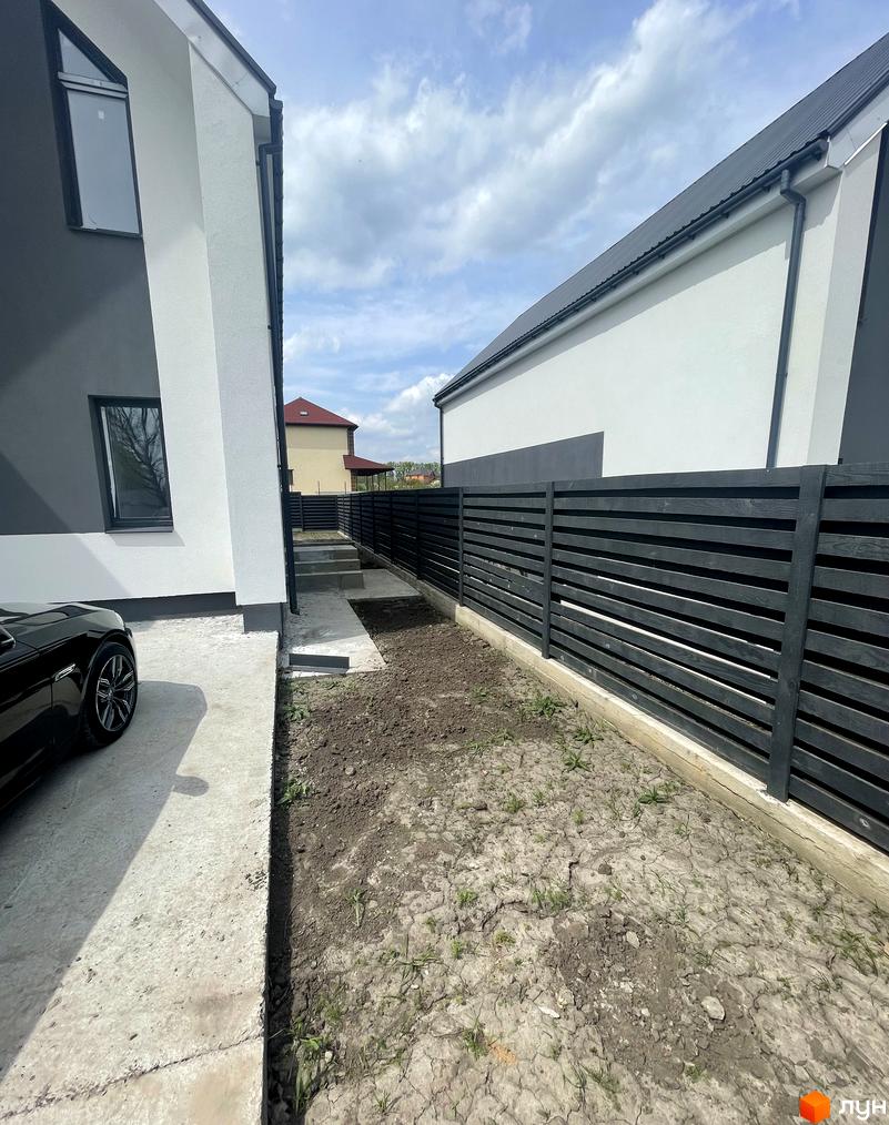 Зовнішній вигляд дуплексів „На Зоряному“ з чорним парканом та бетонною доріжкою. Прибудинкова територія з ґрунтом та травою.