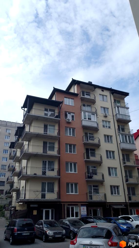 Фасад житлового комплексу на вул. Крушельницької, 35а, з бежево-коричневими стінами та балконами. Перед будинком припарковані автомобілі.