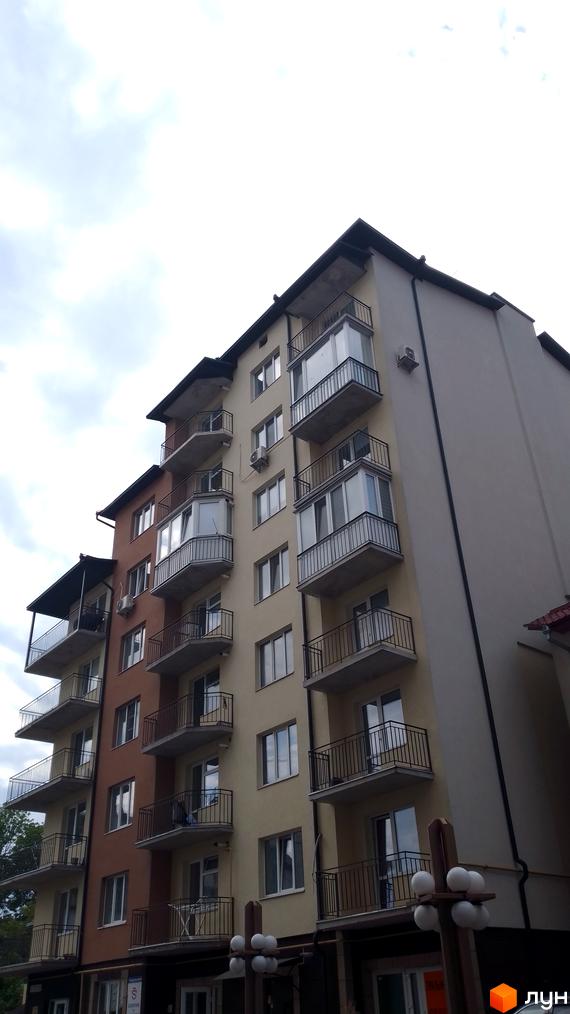 Фасад житлового будинку на вул. Крушельницької, 35а з бежевими та коричневими секціями, відкритими та заскленими балконами. Поруч видно вуличні ліхтарі та зелені насадження.