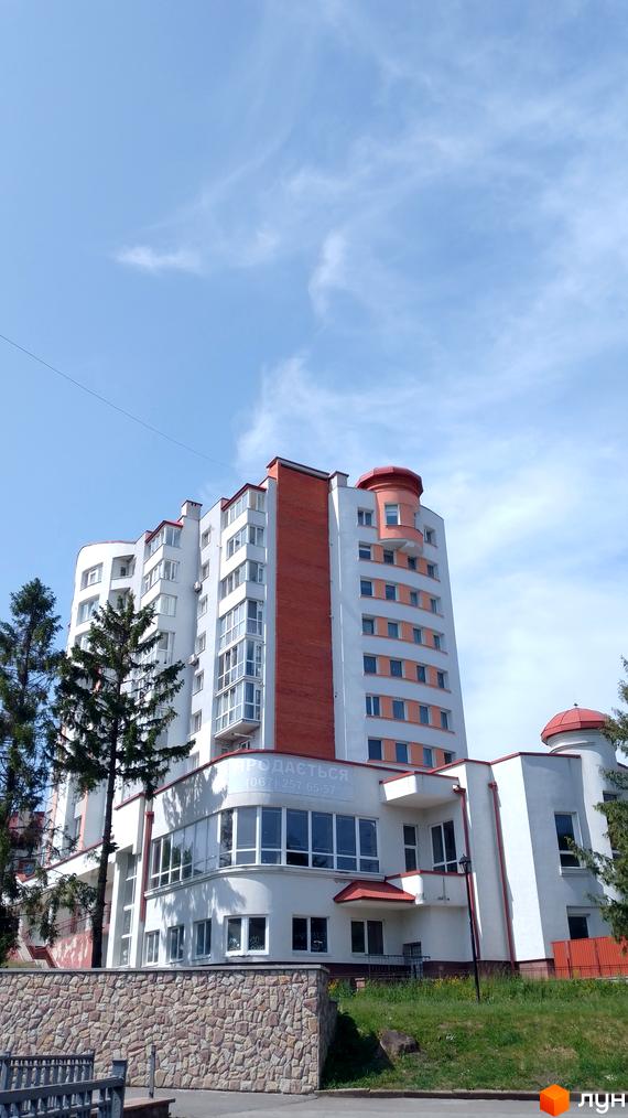 Житловий комплекс Співоче Поле – багатоповерхова новобудова з цегляними та білими фасадами, панорамними вікнами та затишною прибудинковою територією з кам'яною огорожею.