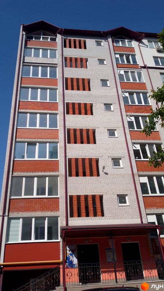 Багатоповерхова новобудова на вул. Рєпіна, 34, з фасадом з світлої цегли, червоними вставками та білими вікнами. Вхідна група має козирок.