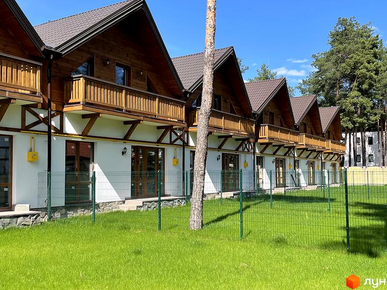 Ряд таунхаусів Desna Residence-2 з коричневими дахами, дерев'яними фасадами та балконами. Перед будинками зелений газон і сосни.