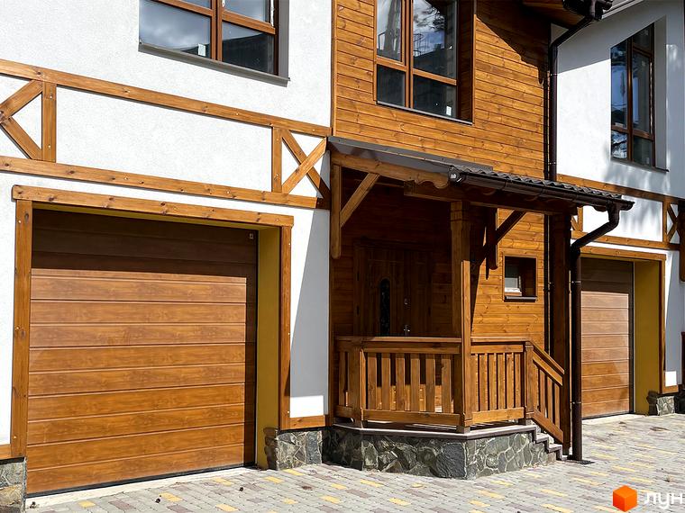 Таунхауси Desna Residence-2: двоповерховий будинок з дерев'яним оздобленням, білими стінами та гаражними воротами. Прибудинкова територія вимощена бруківкою.