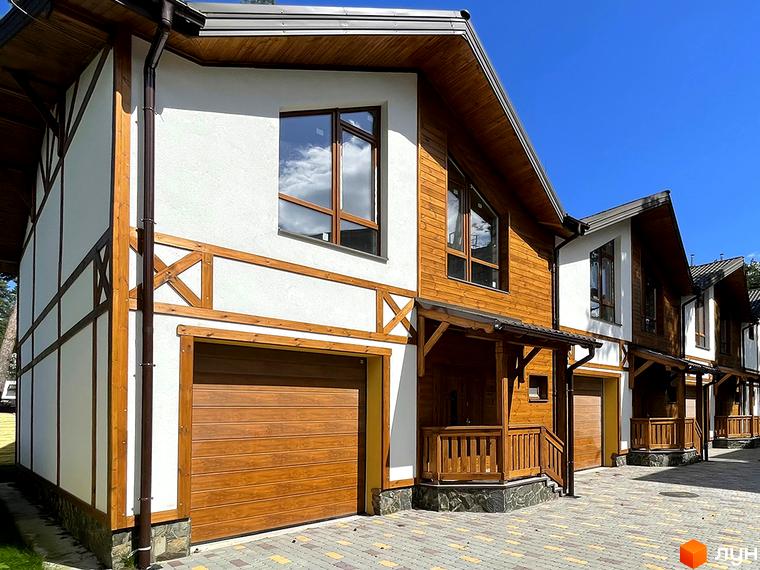 Таунхауси Desna Residence-2 з білими стінами, дерев'яними елементами та коричневими гаражними воротами. Прибудинкова територія вимощена бруківкою.