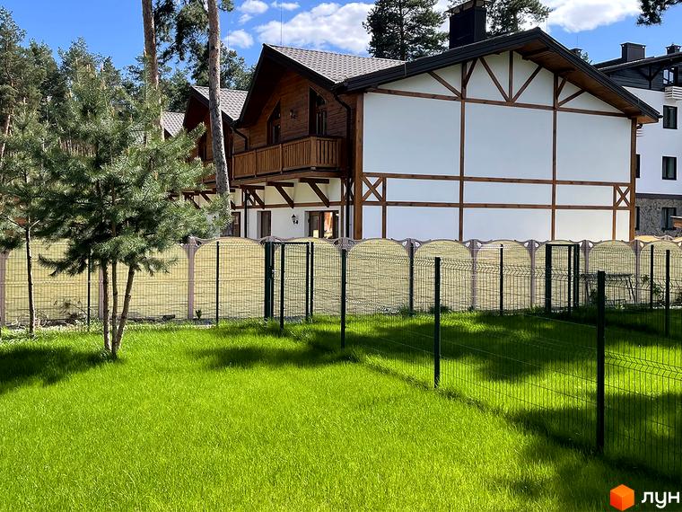 Таунхауси „Desna Residence-2“ з дерев'яними елементами на фасаді та темним дахом. Перед будинками доглянутий газон та зелений паркан.