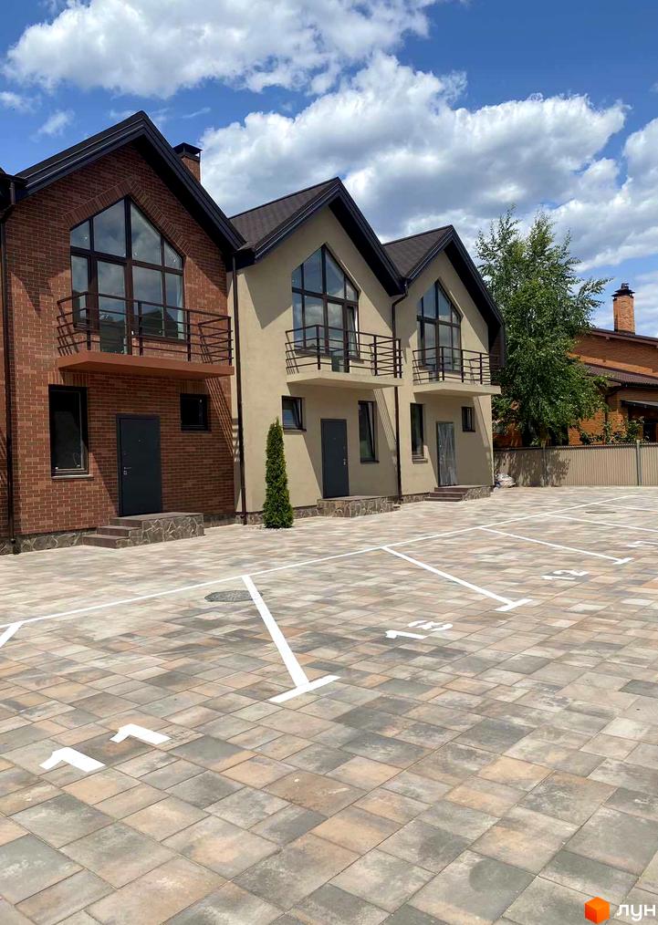 Триповерхові будинки з балконами та панорамними вікнами. На передньому плані парковка з розміткою.