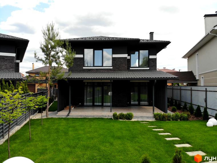 Двоповерховий будинок Котеджного містечка Kulbaba Petropavlivka з темної цегли та великими вікнами. Перед будинком зелений газон з доріжкою та доглянута територія.