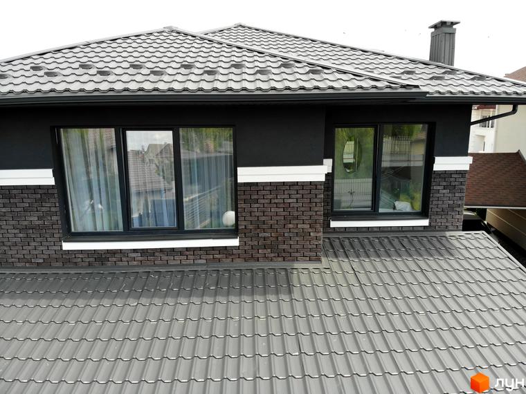 Котеджне містечко Kulbaba Petropavlivka: фасад будинку з темно-сірою черепицею, цегляними елементами та чорними вікнами. Видно частину даху та оточення.