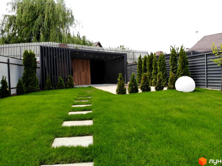 Котеджне містечко Kulbaba Petropavlivka: будівля з темним оздобленням та дерев'яними панелями, на газоні доріжка з плит, туї та біла куля.