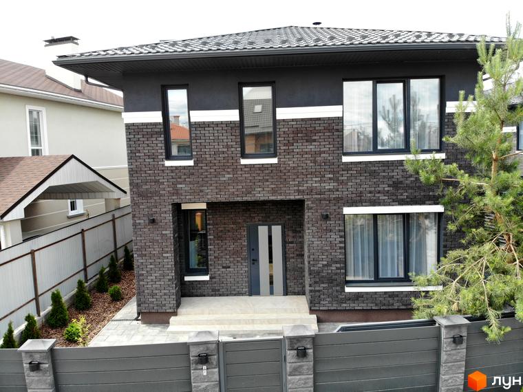 Фасад будинку Котеджного містечка Kulbaba Petropavlivka з темно-сірої цегли та штукатурки, з бруківкою та огорожею.