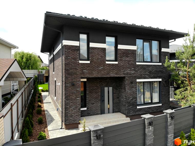 Двоповерховий будинок з темного цегляного фасаду та світлими смугами в КМ Kulbaba Petropavlivka. Прилегла територія має доріжку та зелені насадження.