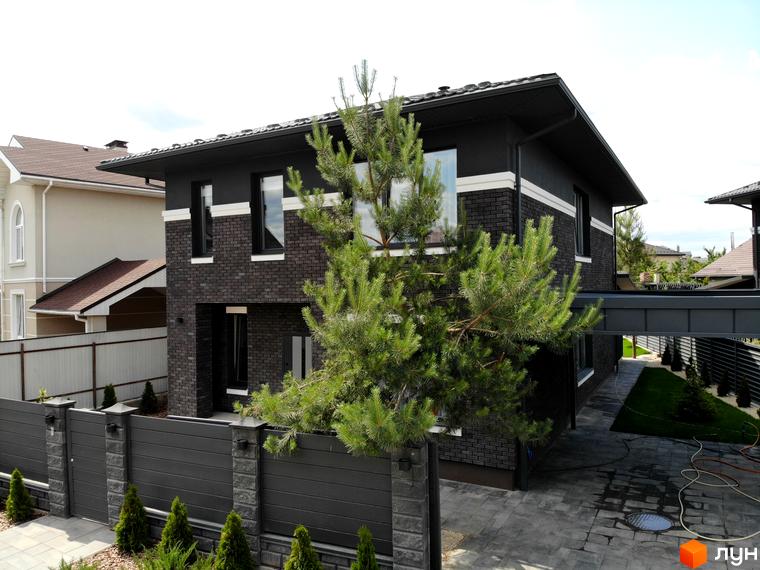 Будинок Котеджного містечка Kulbaba Petropavlivka має фасад з темної цегли та білих смуг. Подвір'я облаштоване бруківкою, зеленими насадженнями та темним парканом.