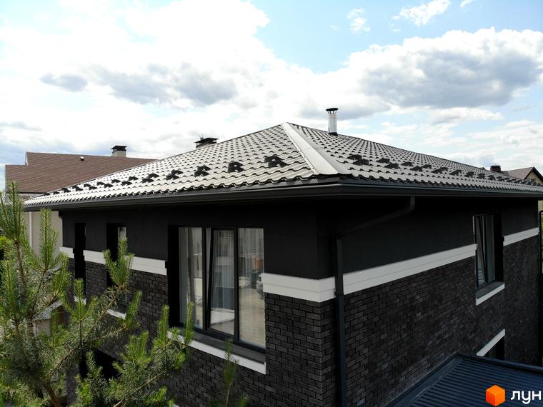 Будинок КМ Kulbaba Petropavlivka з темно-сірою металочерепицею та фасадом з темної цегли і штукатурки з білою смугою.
