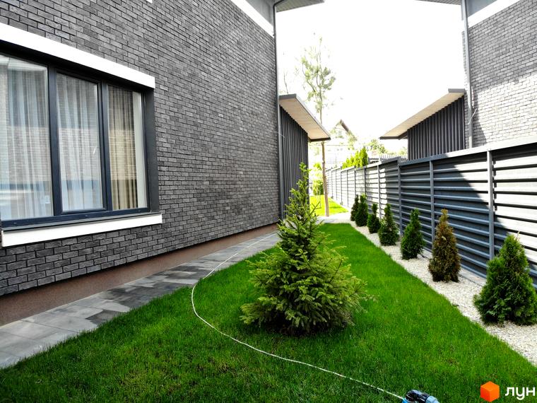 Котеджне містечко Kulbaba Petropavlivka: будинок з темно-сірої цегли та великими вікнами. На ділянці зелений газон, хвойні дерева, доріжка.