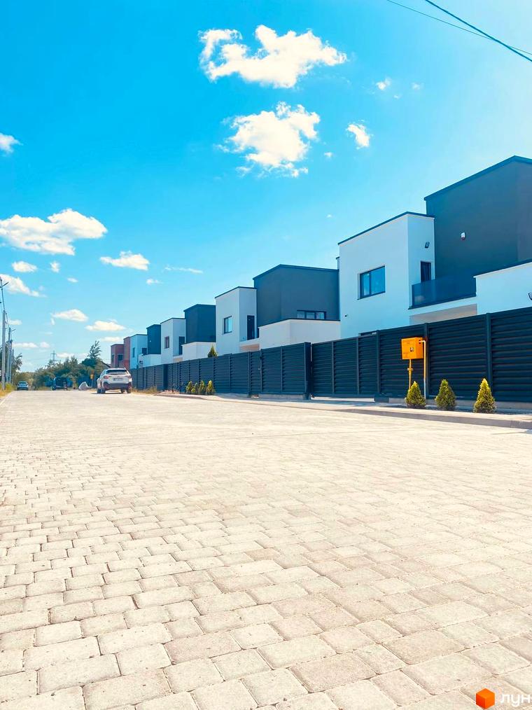 Котеджне містечко PRIDE Residents: ряд двоповерхових будинків з білими та темно-сірими фасадами, перед якими бруківка та темні огорожі.