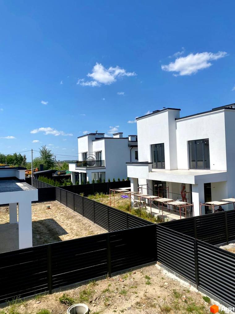 Білі будинки з чорними дахами та вікнами, огороджені чорним парканом. На території видно траву та підготовку до ландшафтного дизайну. КМ PRIDE Residents.