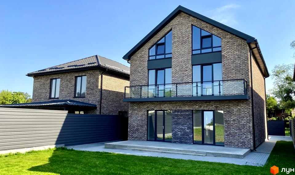 Котеджне містечко КМ Набережний: двоповерхові цегляні будинки з великими вікнами та скляними балконами, зелена галявина та сірий паркан.