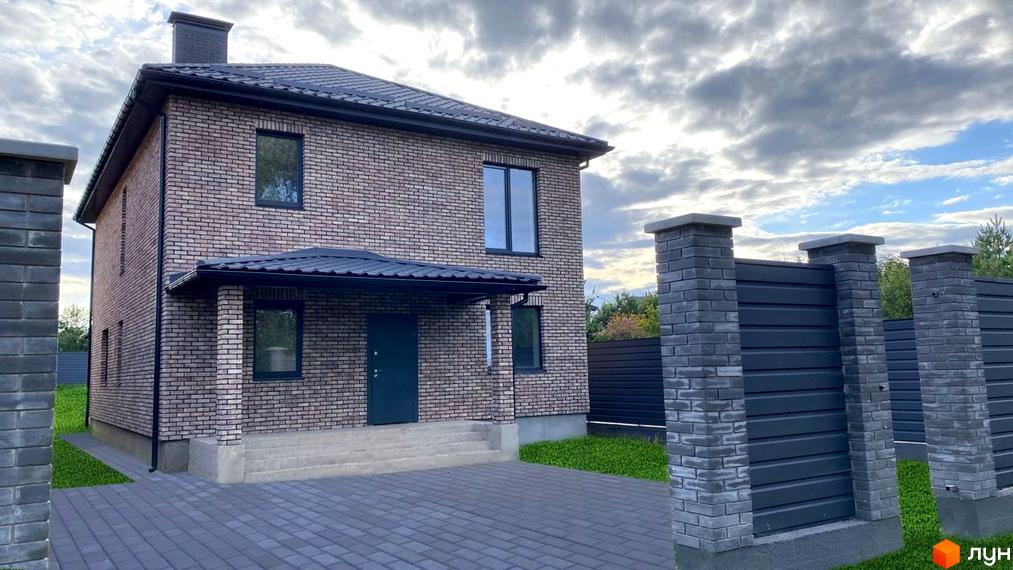 Двоповерховий будинок з цегляними стінами та темним дахом. Перед будинком бруківка та огорожа Котеджного містечка Набережний.