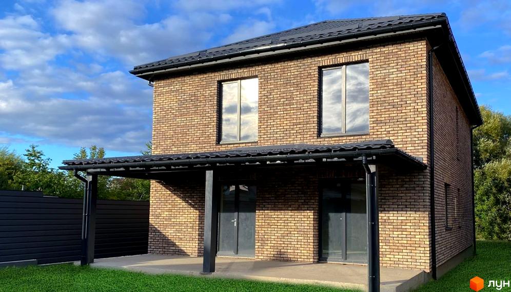 Котеджне містечко КМ Набережний: двоповерховий цегляний будинок з чорним дахом та навісом. Навколо будинку зелена галявина та чорний паркан.
