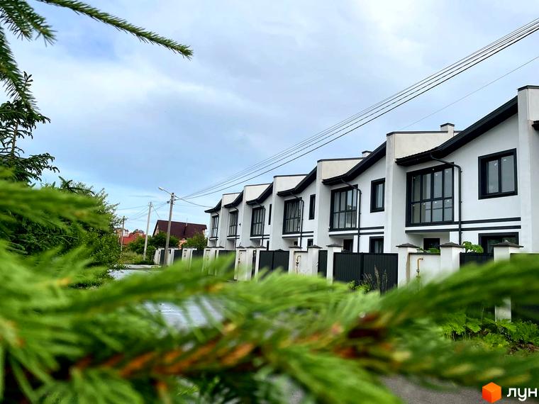 Таунхаус WEST TOWN I: ряд білих будинків з чорними дахами та вікнами, розташованих вздовж дороги із зеленими насадженнями.