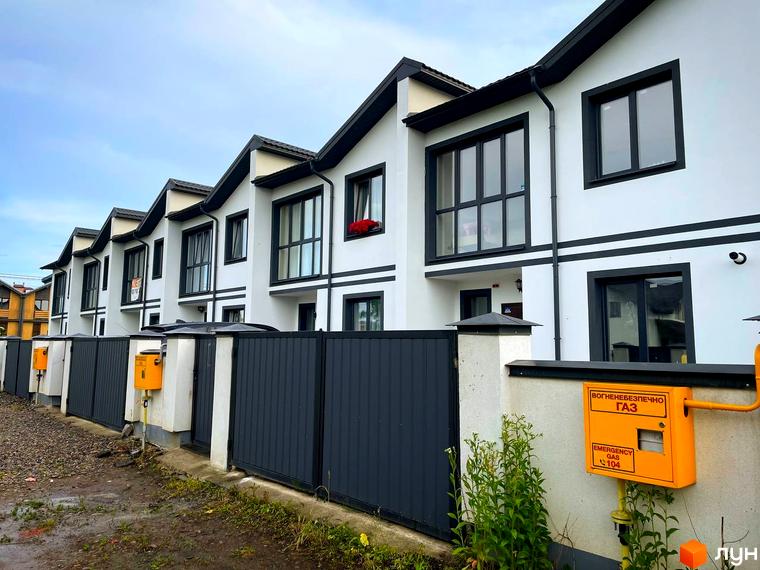 Зовнішній вигляд таунхаусів WEST TOWN III з чорними вікнами та білими стінами. Перед будинками сіра огорожа та жовті газові шафи.