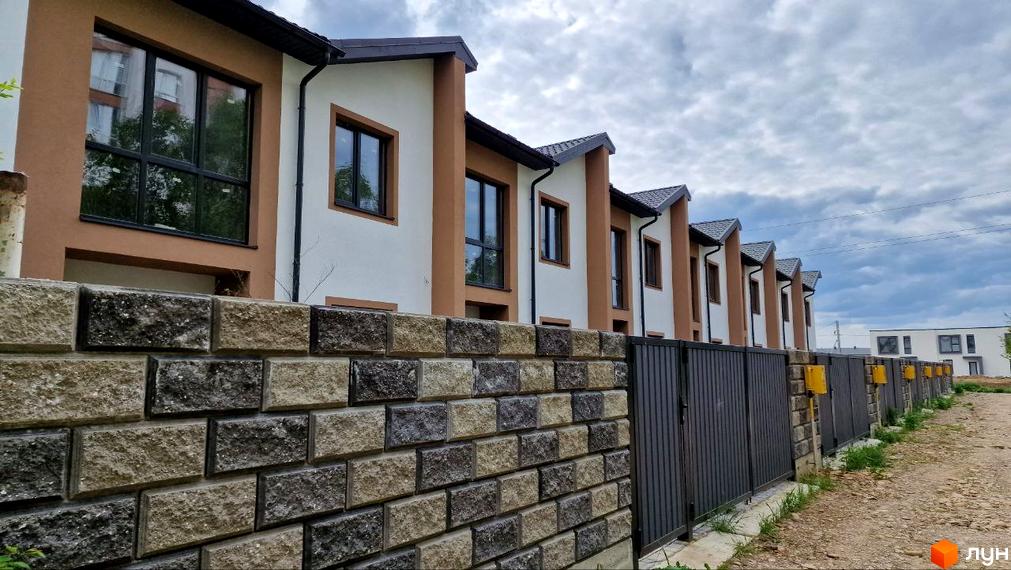 Ряд таунхаусів WEST TOWN IV з білими фасадами та коричневими акцентами. На передньому плані кам'яна стіна та металевий паркан.