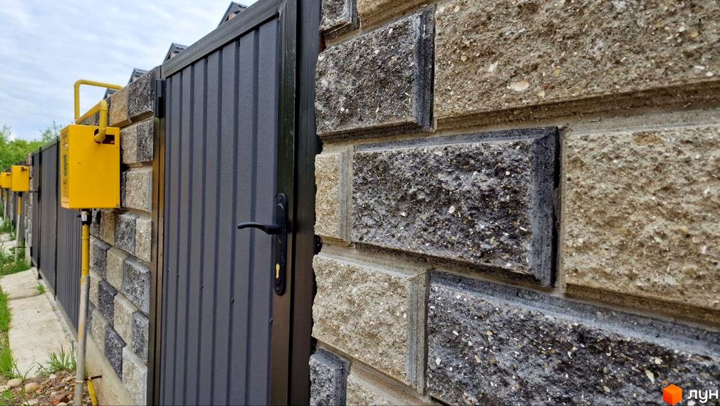 Огорожа Таунхаус WEST TOWN IV з сірих металевих панелей та бетонних блоків, поруч встановлені жовті газові лічильники.