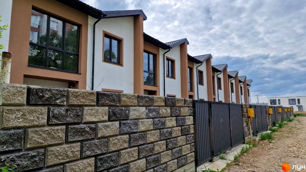 Таунхаус WEST TOWN IV: ряд будинків з біло-коричневими фасадами та чорними вікнами, огорожений кам'яним парканом і металевими воротами.