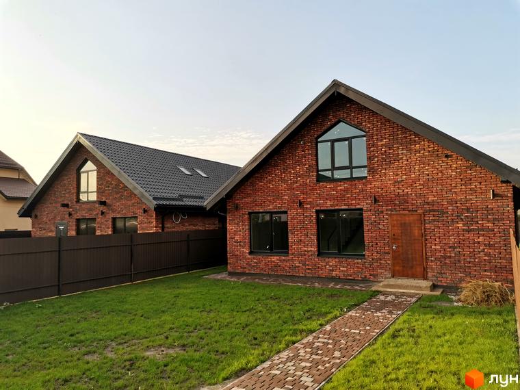 Вигляд цегляного будинку в Котеджному містечку Західна Баварія. Навколо будинку зелений газон та доріжка з тротуарної плитки.