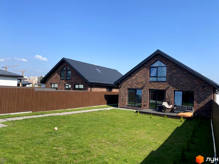 Зображення двоповерхового будинку з червоної цегли в Котеджному містечку Західна Баварія. Навколо будинку зелений газон.