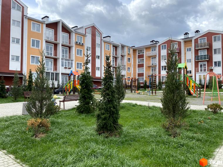 Будівлі житлового комплексу Амстердам з фасадами в помаранчевих та коричневих тонах. На прибудинковій території дитячий майданчик та зелені насадження.