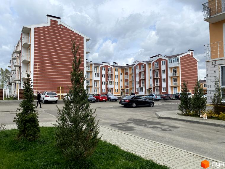 Багатоповерховий будинок ЖК Амстердам з балконами та паркуванням. На передньому плані зелені насадження та тротуар.