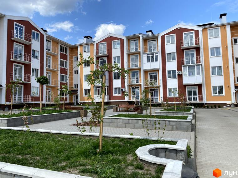 Багатосекційний будинок ЖК Амстердам з фасадом в теплих кольорах. Озеленена прибудинкова територія з газонами, деревами та доріжками.