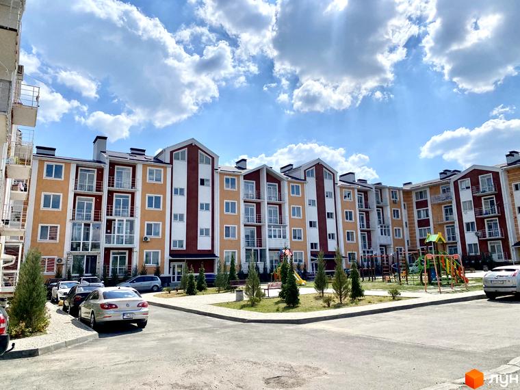 Зовнішній вигляд багатоповерхового будинку ЖК Амстердам з балконами та вікнами, поруч прибудинкова територія з паркуванням та дитячим майданчиком.
