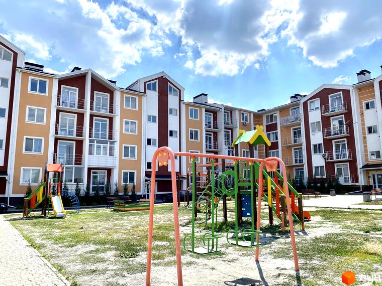 Житловий комплекс Амстердам з дитячим майданчиком на фоні сонячного неба. Яскраві фасади будинку з балконами та вікнами створюють затишну атмосферу для життя.