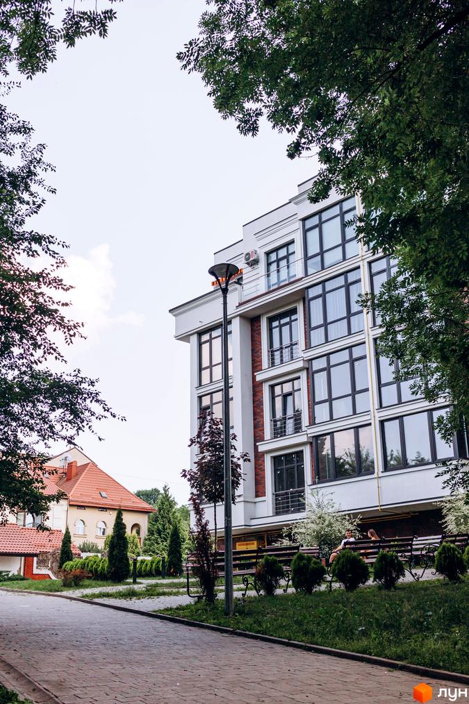 Клубний будинок Rezydencja „Zalizna Voda” з великими вікнами та цегляними вставками, поруч доглянута прибудинкова територія з лавками та деревами.