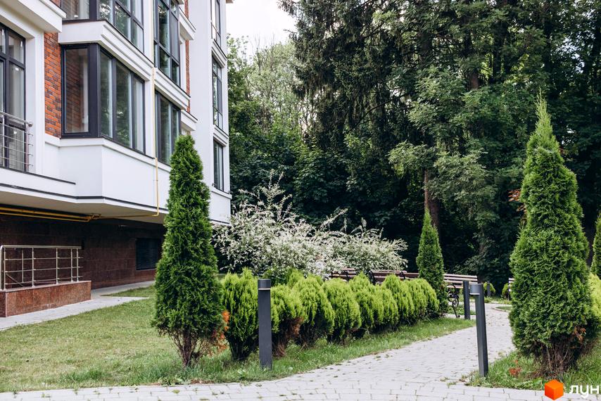 Клубний будинок Rezydencja „Zalizna Voda” з цегляним фасадом та великими вікнами, оточений доглянутою прибудинковою територією з деревами та кущами.