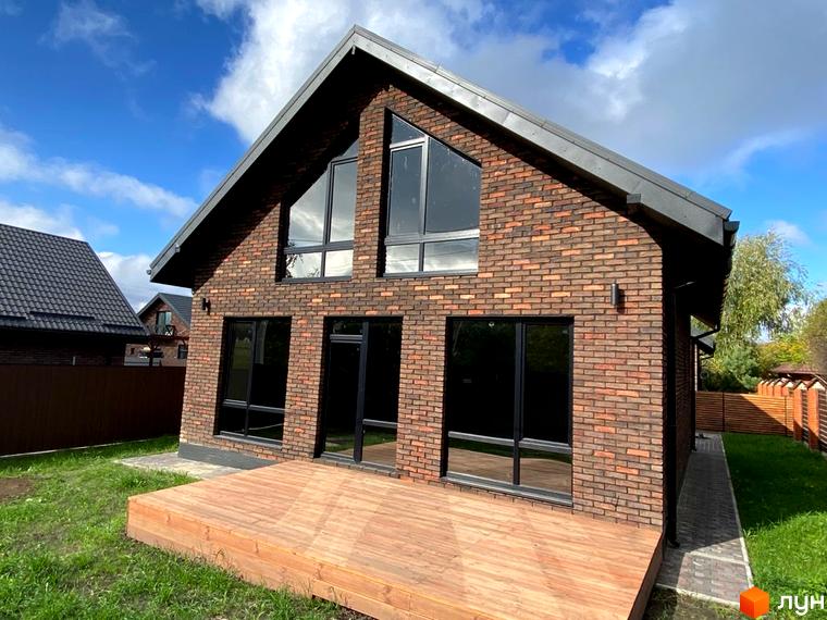 Котеджне містечко КМ Одноповерховий Київ - Білогородка. Зовнішній вигляд цегляного будинку з великими вікнами та дерев'яною терасою, зелена галявина.