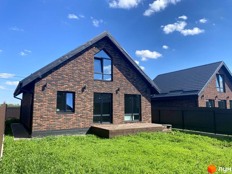 Котеджне містечко КМ Одноповерховий Київ - Білогородка. Фасад будинку з коричневої цегли, великі вікна, дерев'яна тераса та зелений газон.