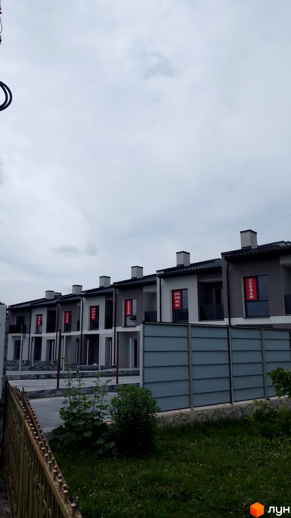 Ряд нових таунхаусів сірого та білого кольору з темними дахами, на вікнах таблички 